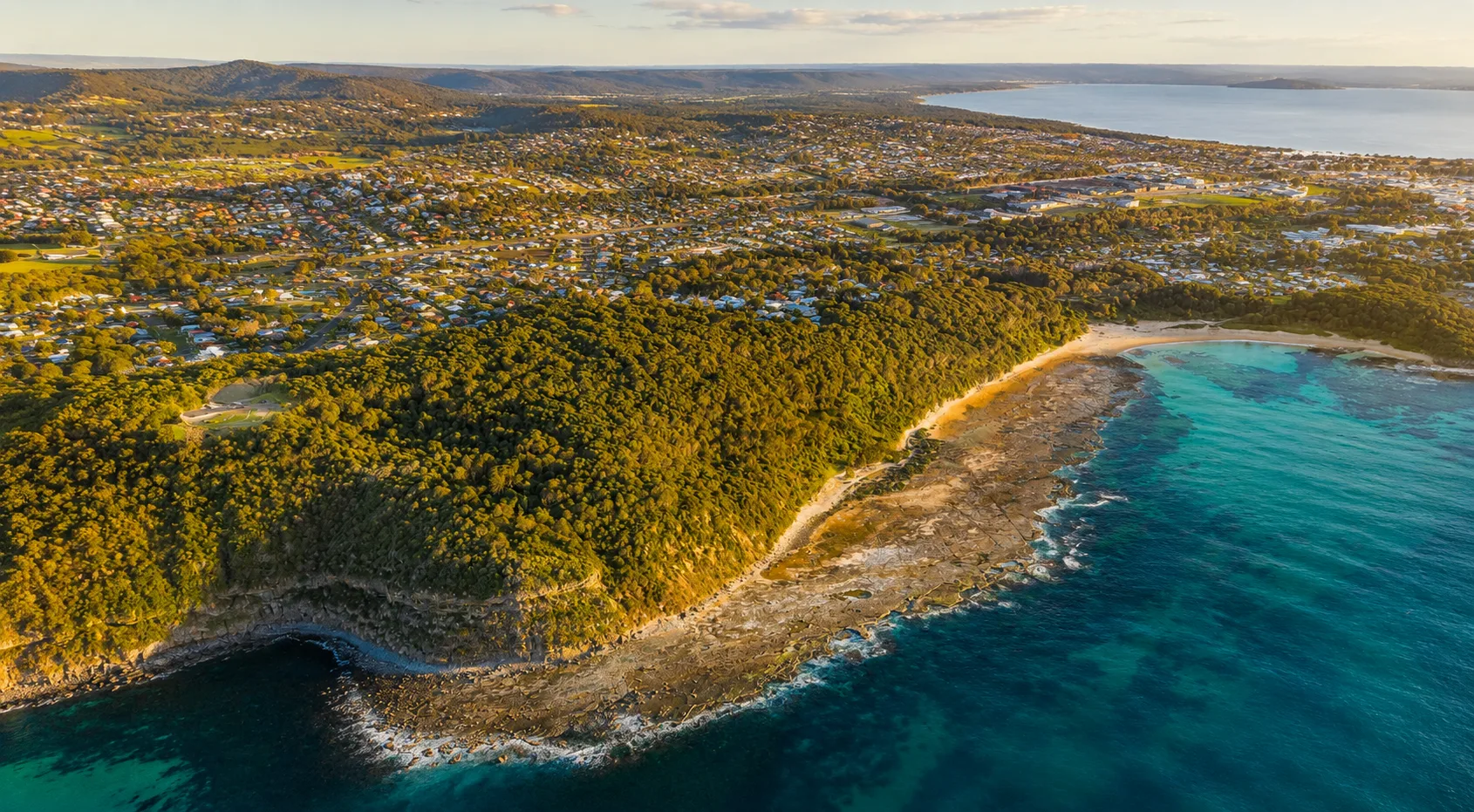 Aerial view across Bateau Bay's coastline, Wyrrabalong National Park and homes at golden hour