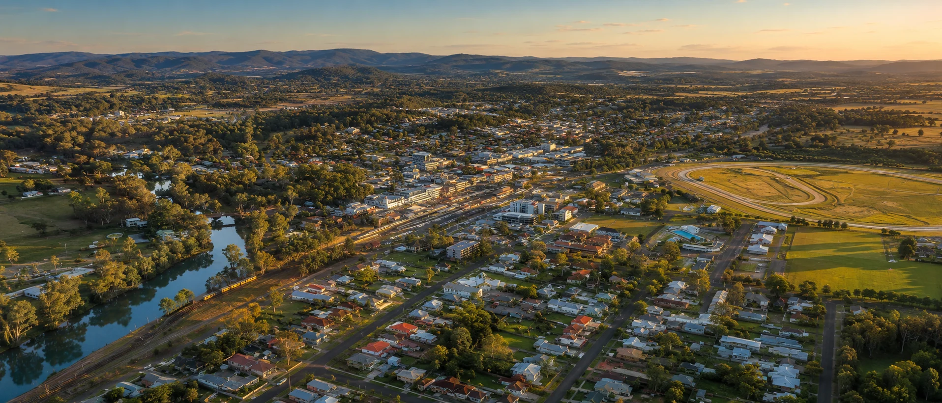 Aerial panorama of Wyong town centre, river, railway, racecourse and surrounding hills at sunset