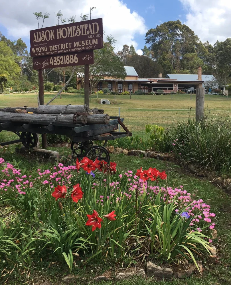 Alison Homestead and Wyong District Museum behind its heritage sign, garden and timber wagon
